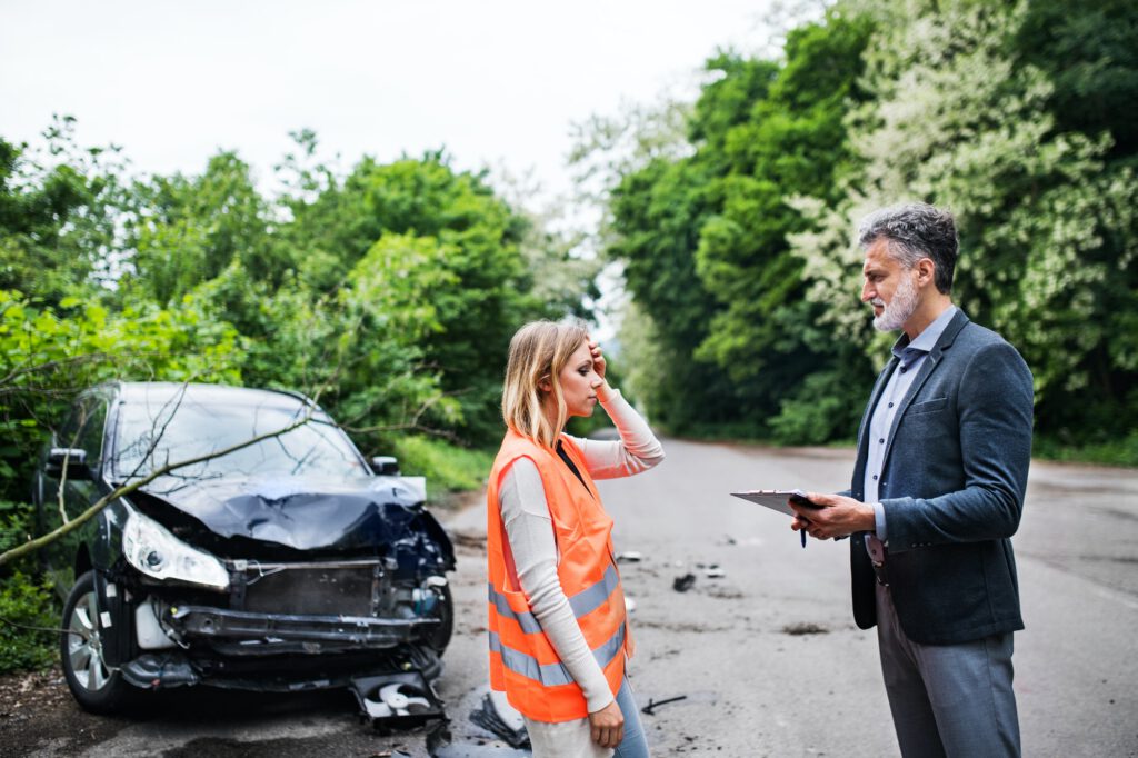 An insurance agent talking to a woman driver by the car on the road after an accident.