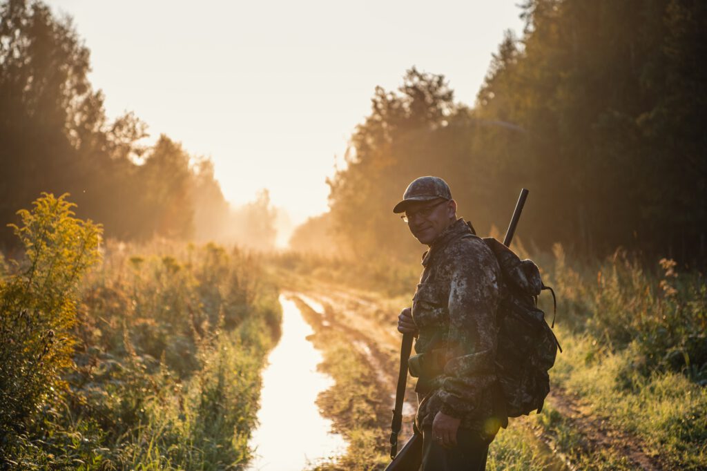 Bird Hunter at Sunrise going for hunt in a forest with his shotgun rifle